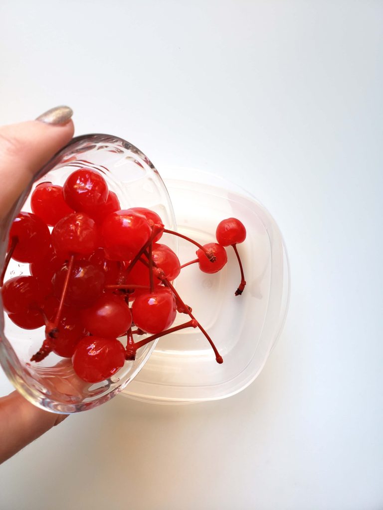 Clear bowl of maraschino cherries being poured into a clear container. 