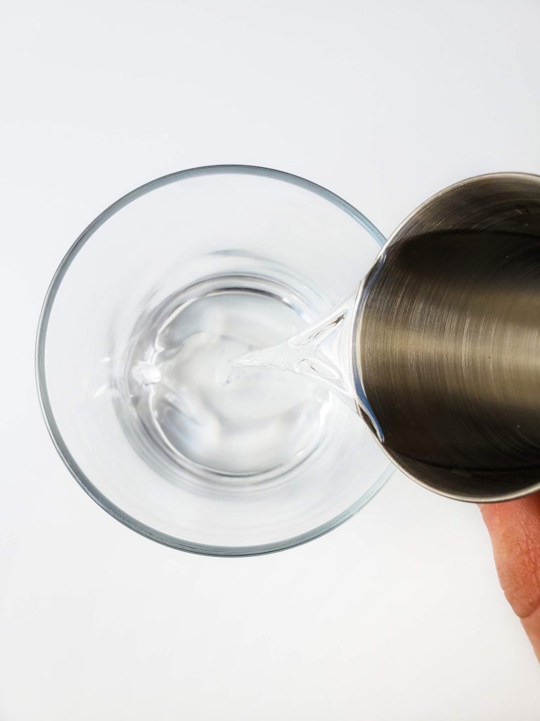 Above view of person adding pineapple vodka in clear glass. 