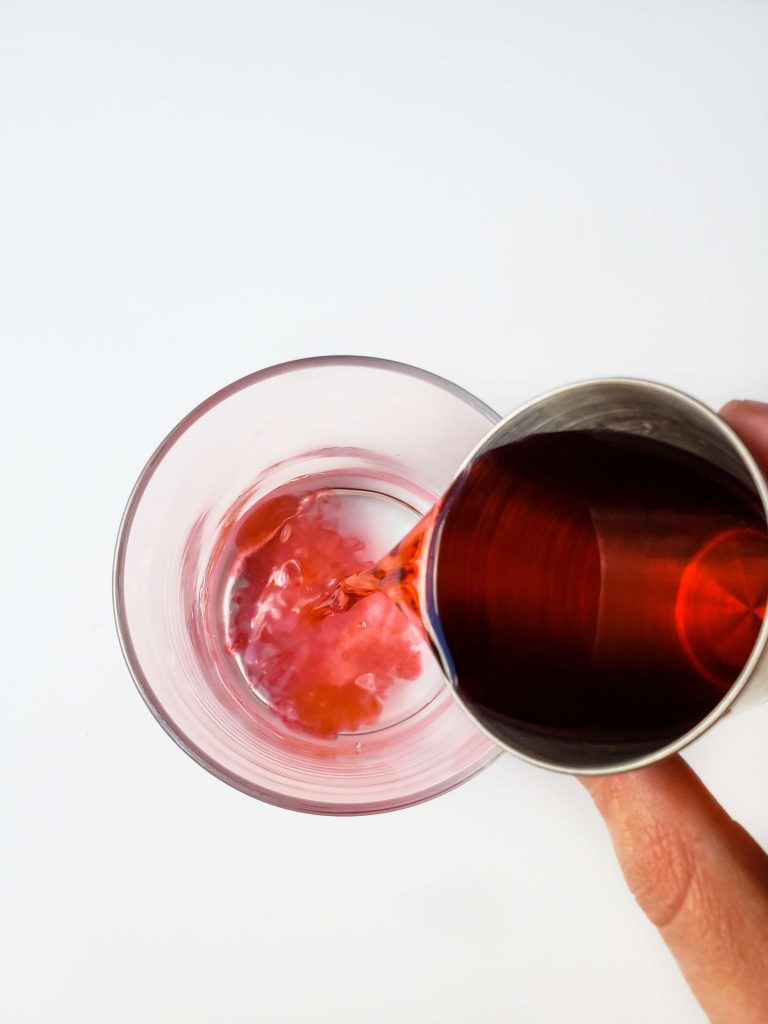 Above view of someone adding cherry liqueur to the cocktail