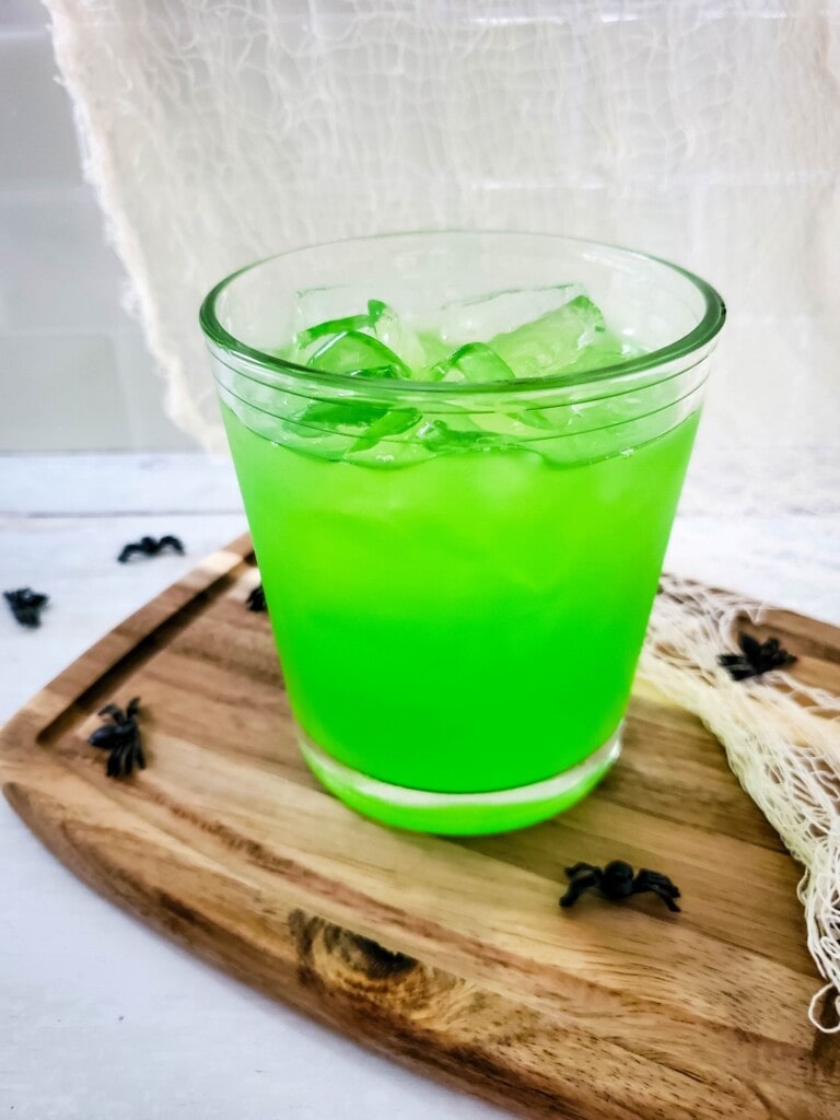 Close up of clear glass with a bright green drink with ice in it. 