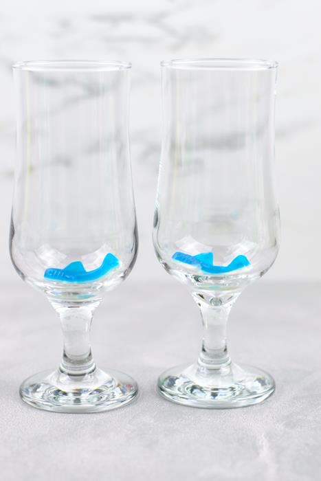 Two tall clear glasses with a single blue shark gummy at the bottom. 