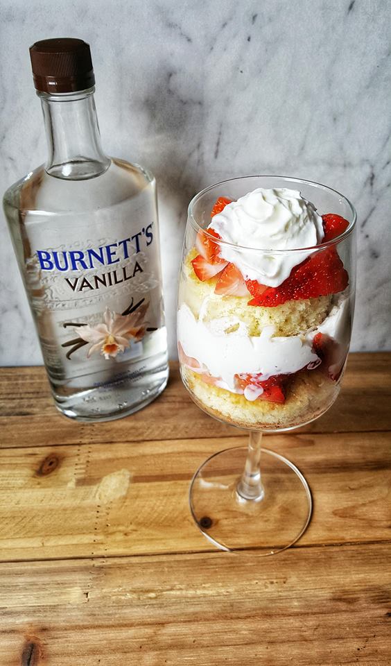 Burnett's Vanilla alcohol bottle next to strawberry desert in a stem glass
