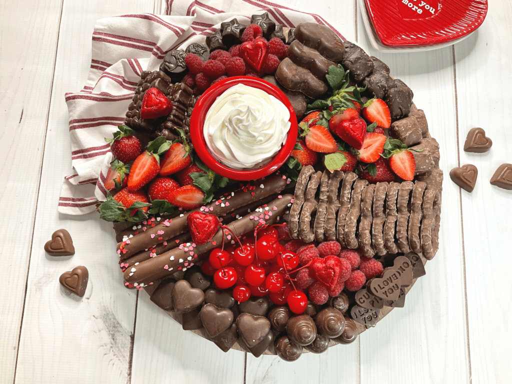 completed charcuterie board with cherries, strawberries, raspberries, homemade peanut butter chocolate hearts, chocolate hearts, chocolate covered pretzels, and a bowl of cool whip. 