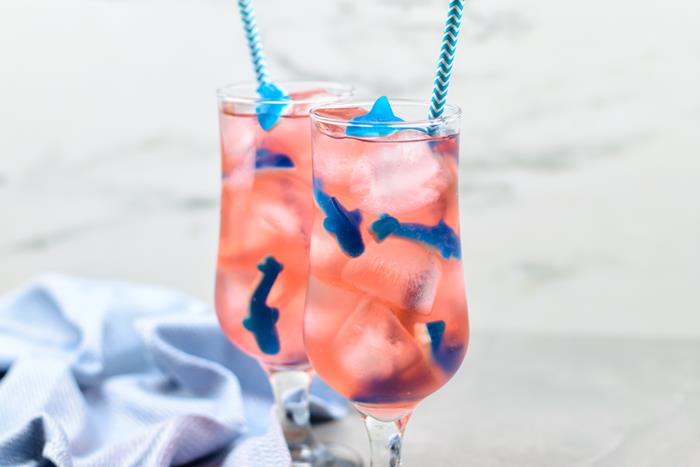Close up of pink liquid with shark gummies, ice, and blue straws sticking out. 