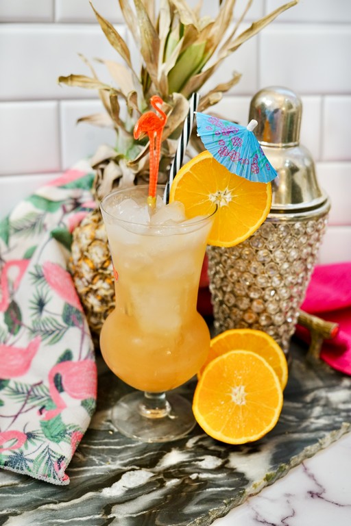 Tall clear glass with a flamingo, paper umbrella, and orange slice as garnish. 