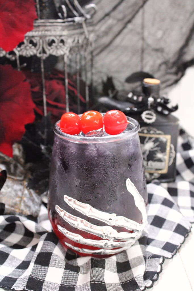 Black Magic Cocktail with Halloween décor in the background on a black and white table cloth. 