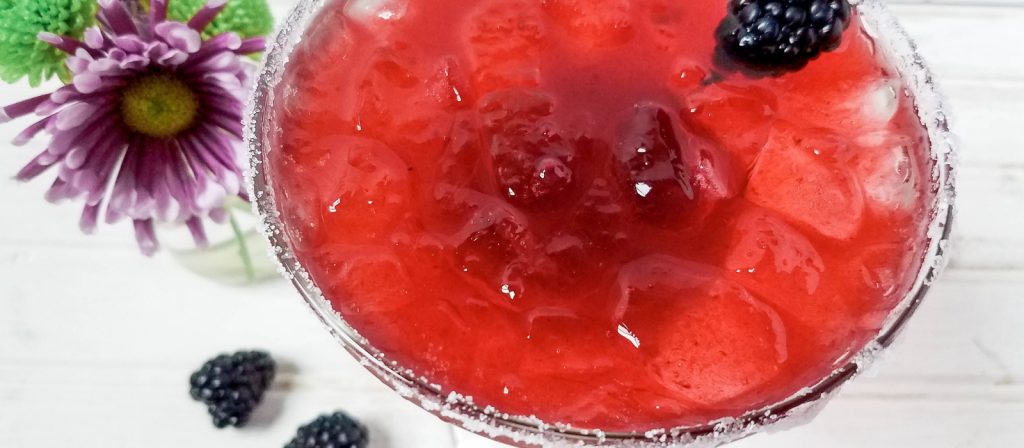 Close up of a Red margarita with a blackberry garnish on a wh