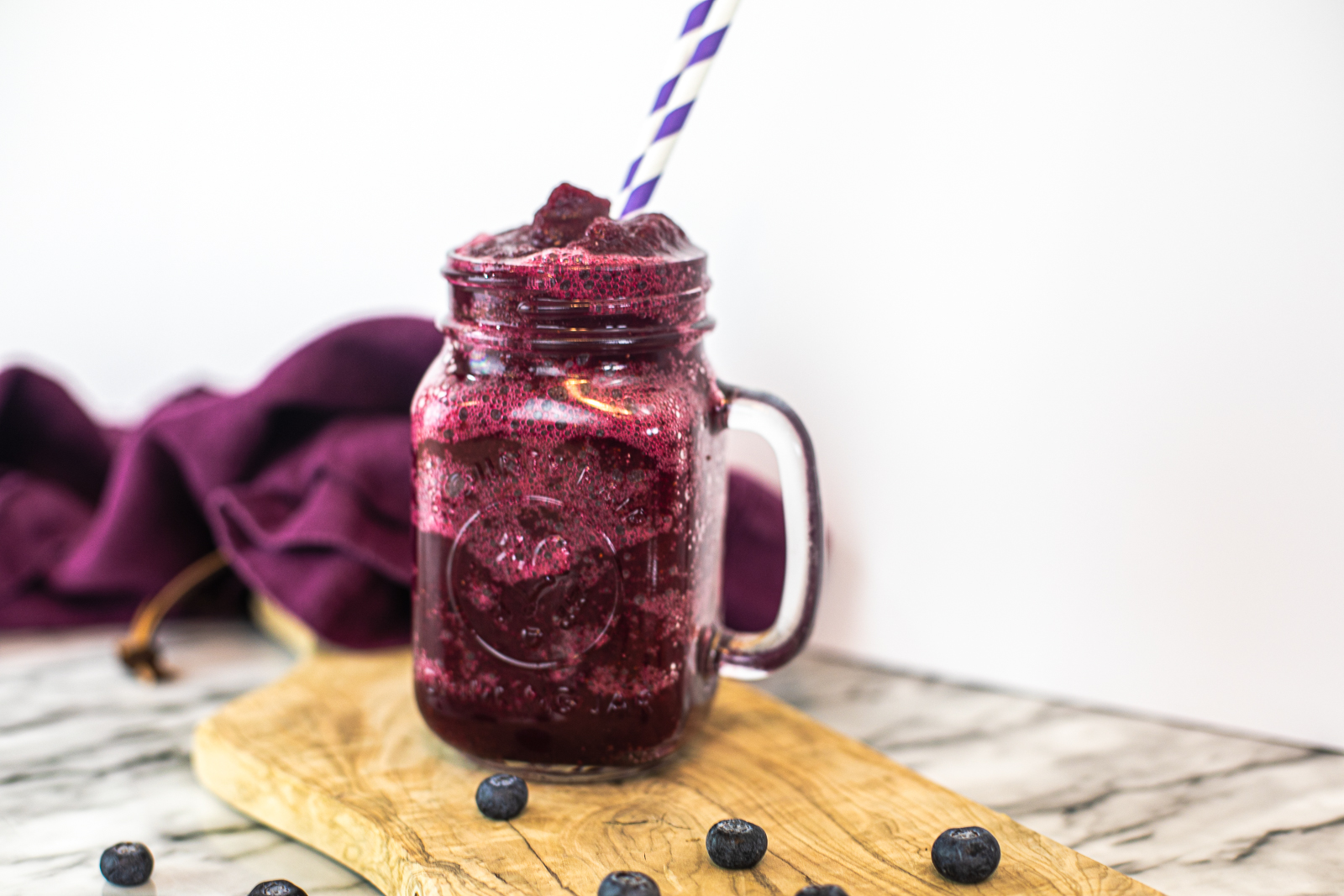 Blended Blueberry Daiquiri on a wooden slab with a purple tea towel in the background. 