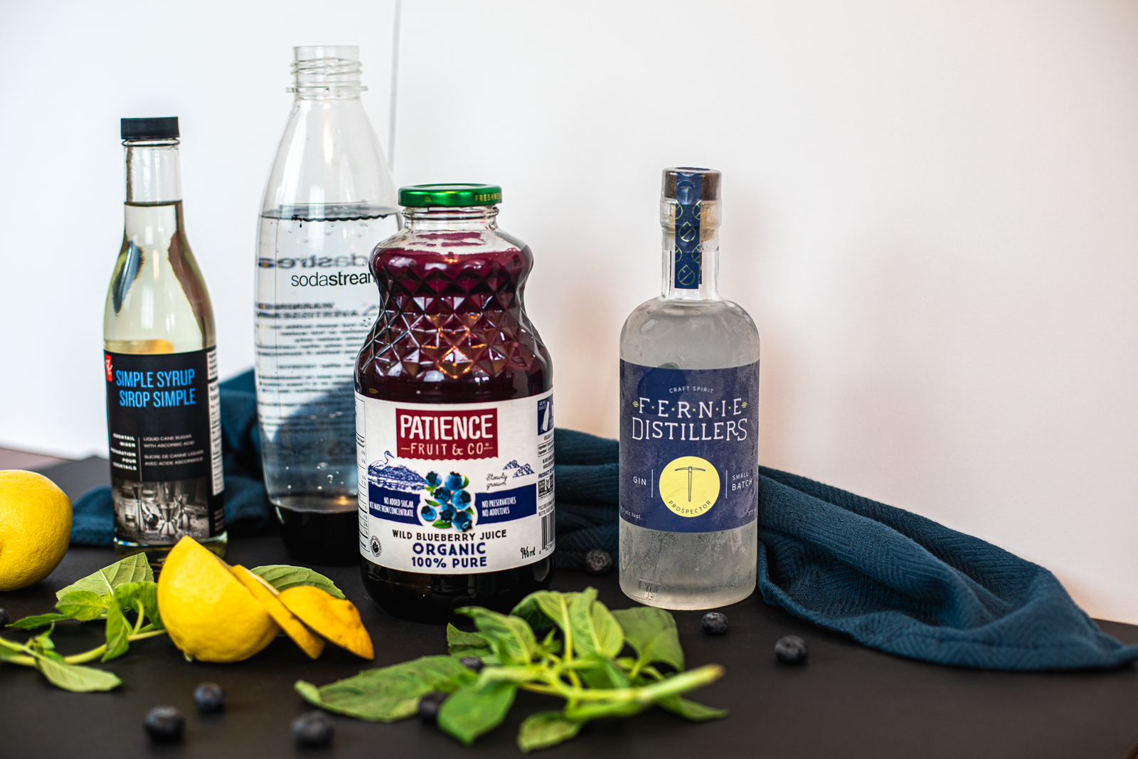 Ingredients needed to make cocktail: simple syrup, soda water, blueberry juice, gin, fresh lemon, basil, and blueberries. 