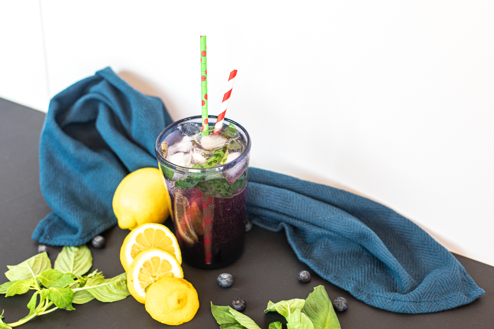 Blueberry Basil Smash with two straws in it, ice, basil and blueberries as garnish. 