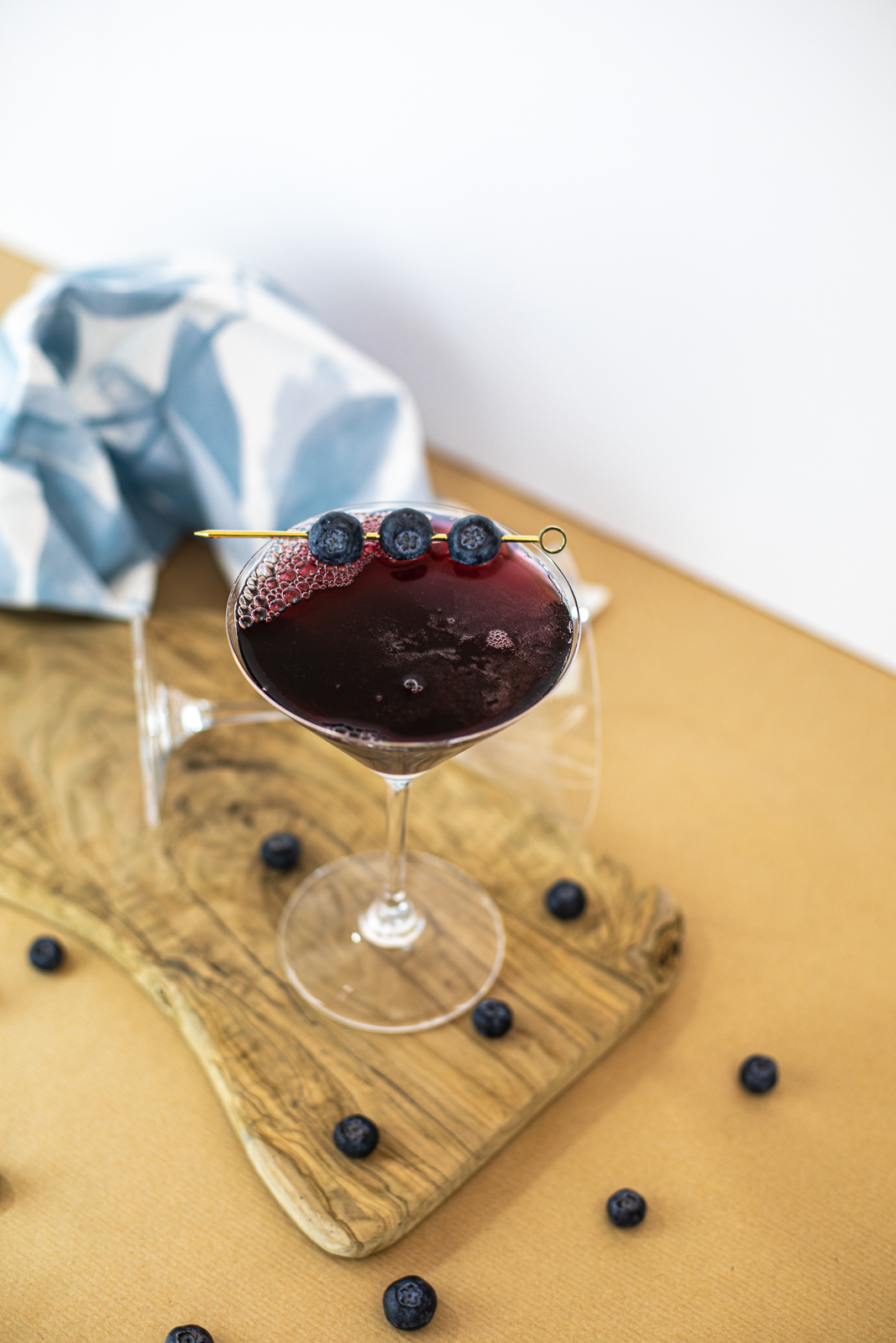 Abovew view of cocktail with three blueberries as garnish on golden stick. 