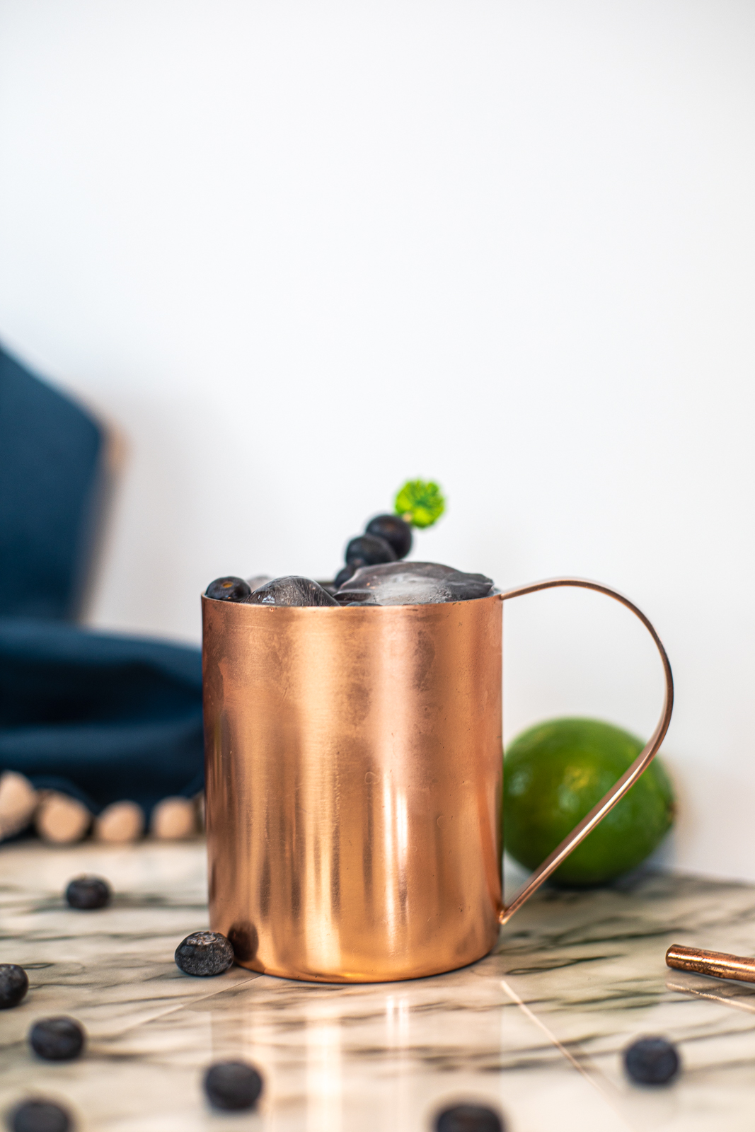 Close up of a copper mug with bueberries sticking out of it. 