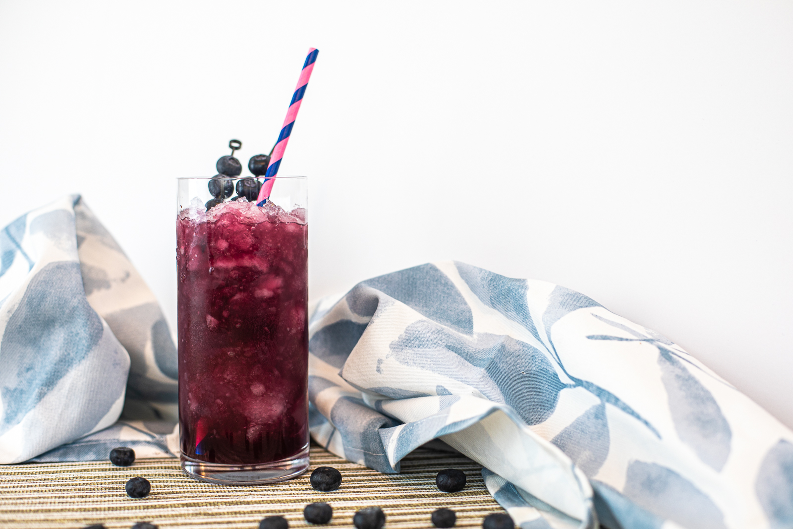 ice and dark purple colored drink in a tall glass with straw and fresh blueberries. 