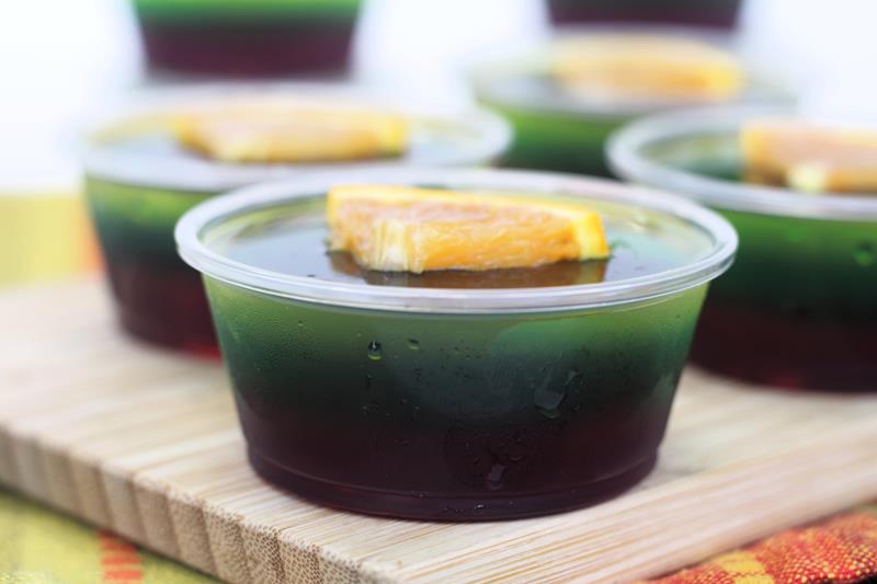 chilled green and purple jello shooter with an orange slice 
