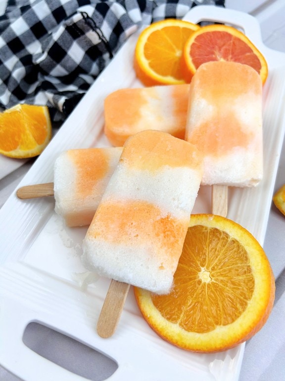 White serving tray with four popsicles on it with orange slices. 