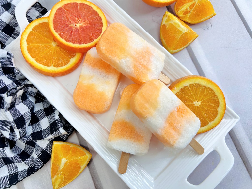 Cool Down This Summer with Boozy Orange Creamsicle Popsicles - white tray plate with four popsicles and orange slices beside it. 