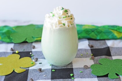 shamrock shake in clear glass topped with whipped cream and green sprinkles 