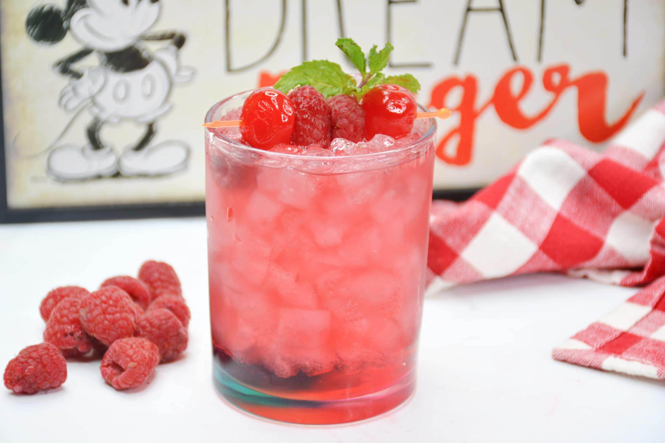 Canadian Victorian Raspberry Cocktail, glass with red drink with lots of ice, raspberries, cherries and mint on top as garnish 