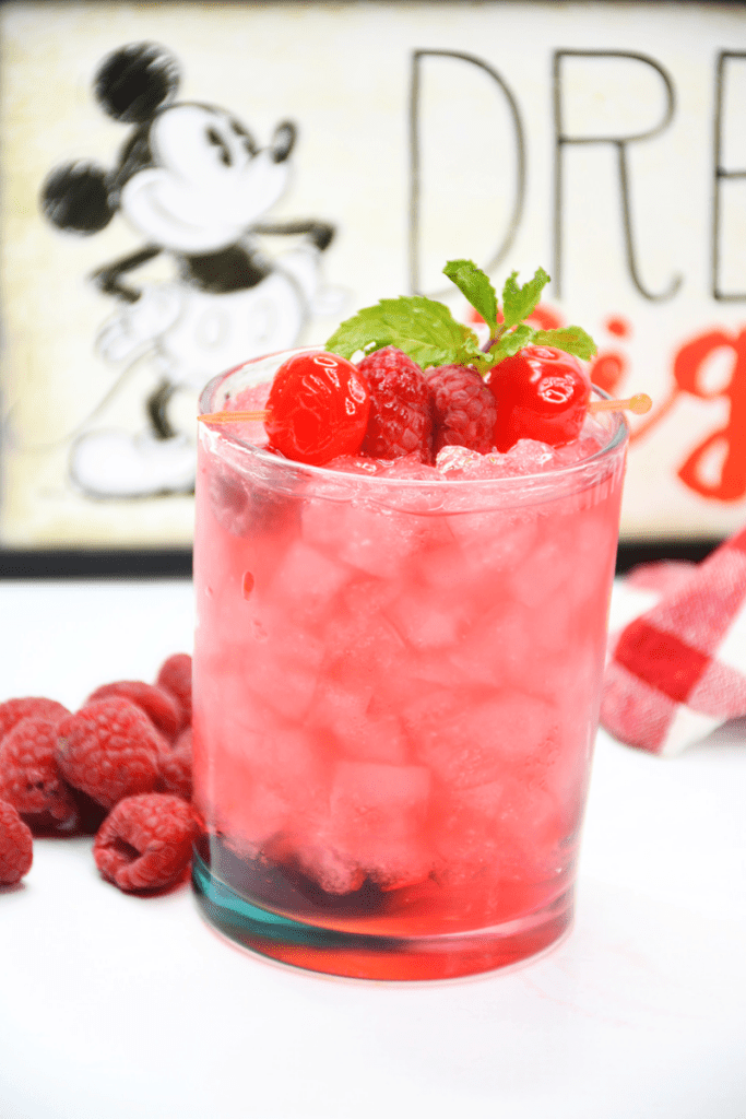 cocktail with garnish and fresh raspberrries beside it 