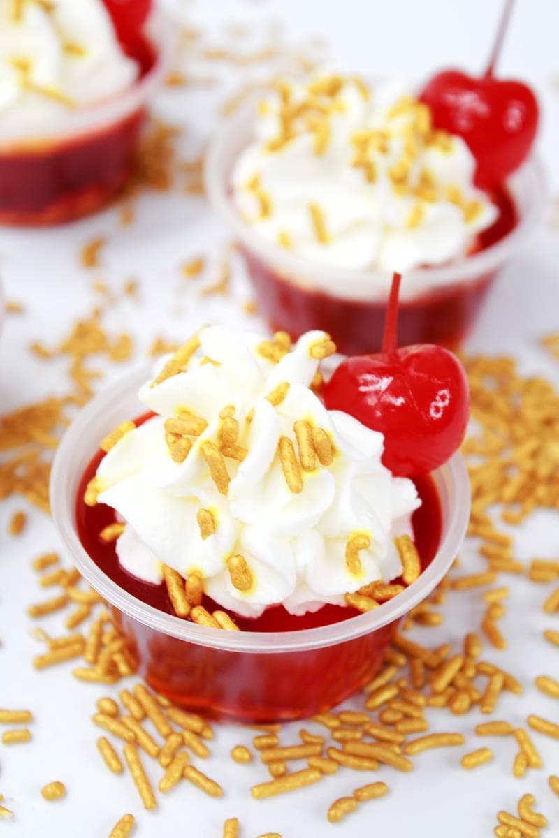 Red jello shooter in a plastic cup with spinkles, whipped cream and a cherry
