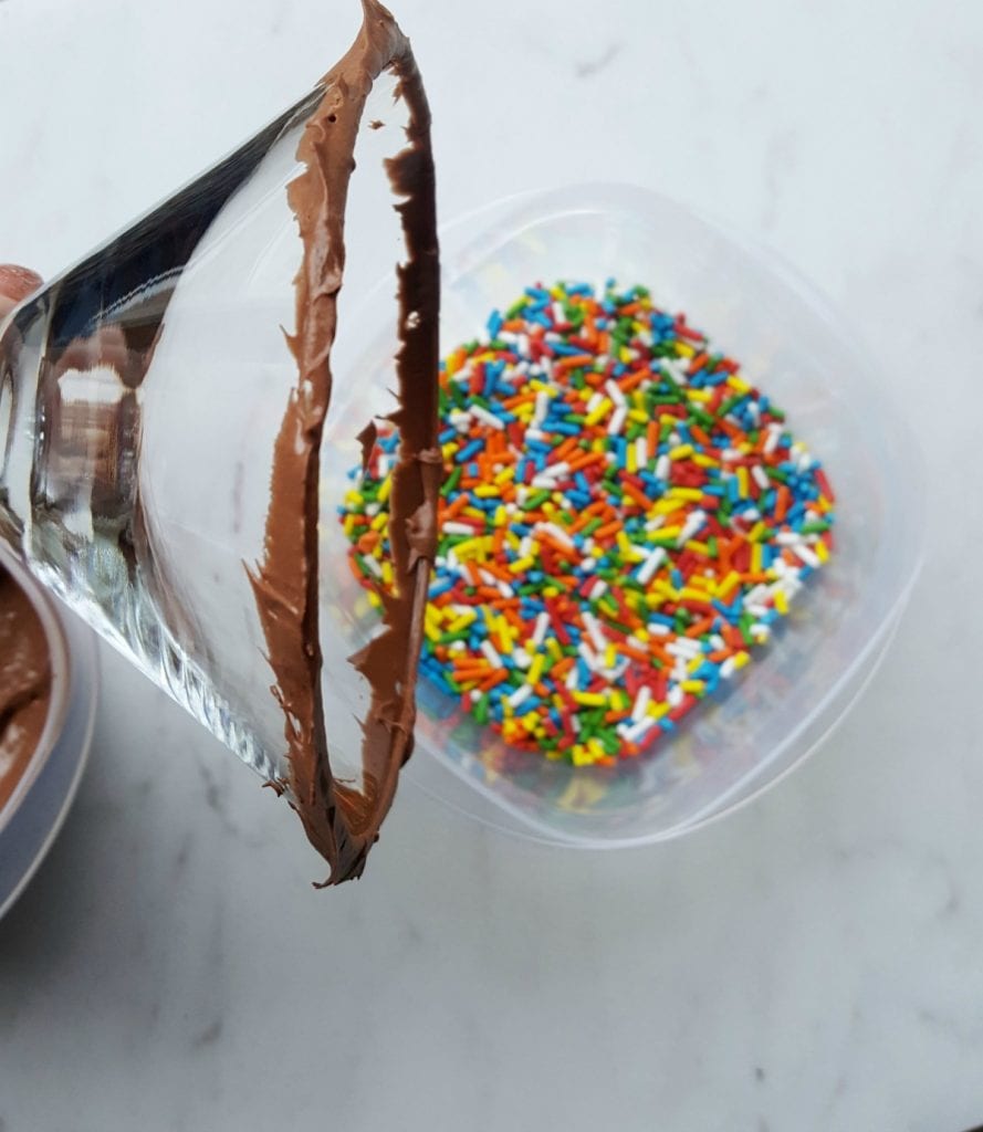 chocolate frosting rimmed martini glass near container full of multi colored sprinkles 