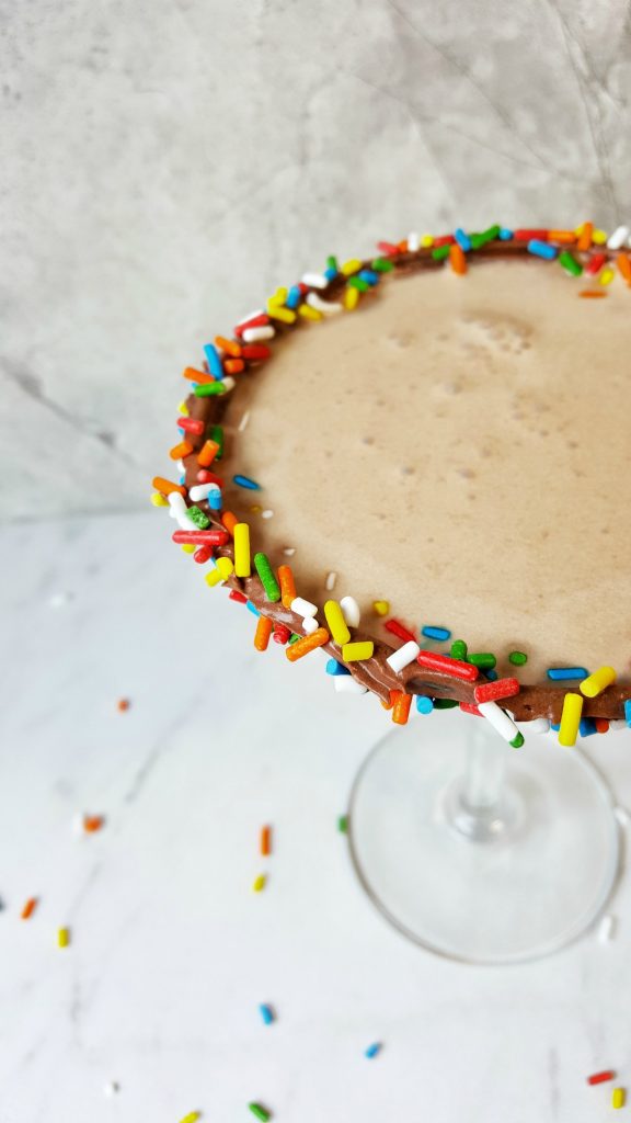 close up of foamy chocolate cocktail with chocolate frosting rim with colorful sprinkles 