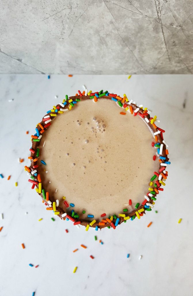top view of cocktail, foamy chocolate drink with sprinkles lined rim 