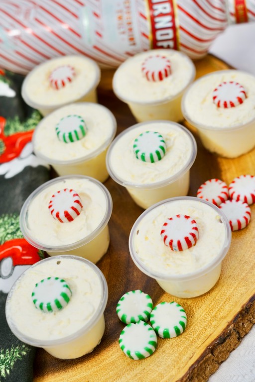 close up of pudding shots with red and white peppermint candies on some and green and white peppermint candies on other. 