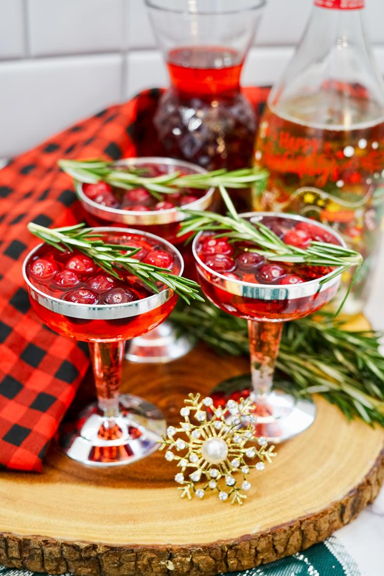 Christmas Mimosa close up showing red drink with rosemary and cranberries in them. 