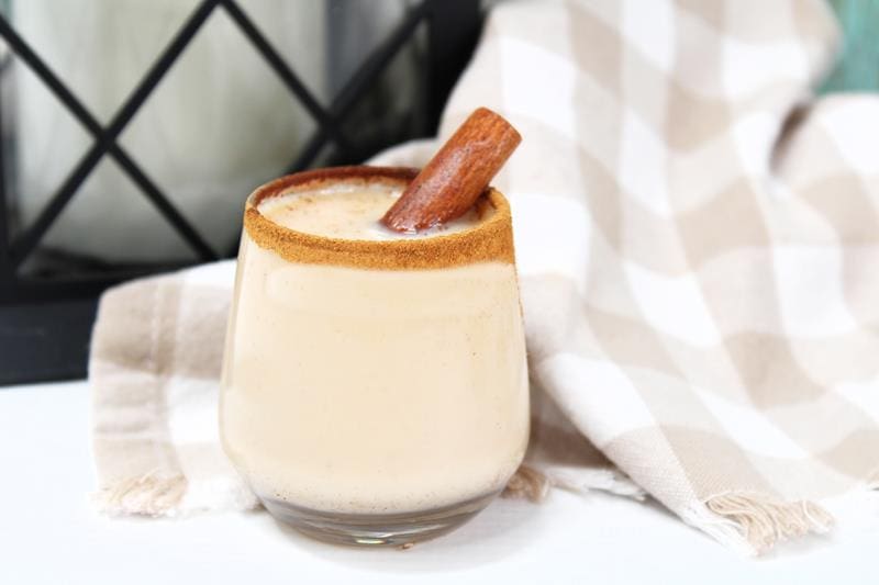 clear glass filled with creamy drink with cinnamon around rim and cinnamon stick sticking out. 