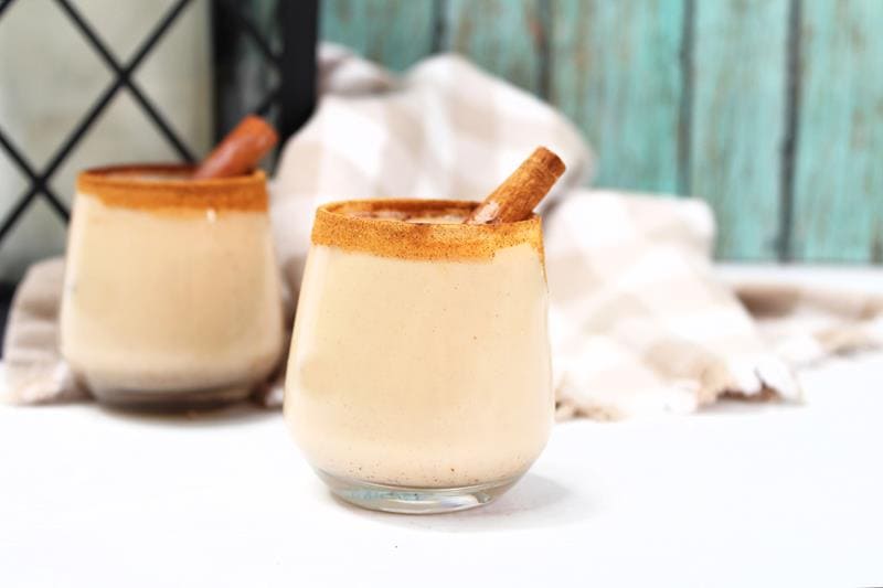 Two completed Churro shots with cinnamon around the rims of clear shot glasses with a full cinnamon stick sticking out of the drinks. 