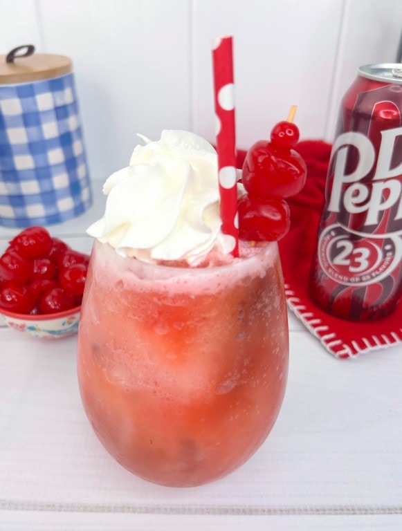 Dirty Dr. Pepper Frozen Rum Slush close up with whip cream, and cherries. 