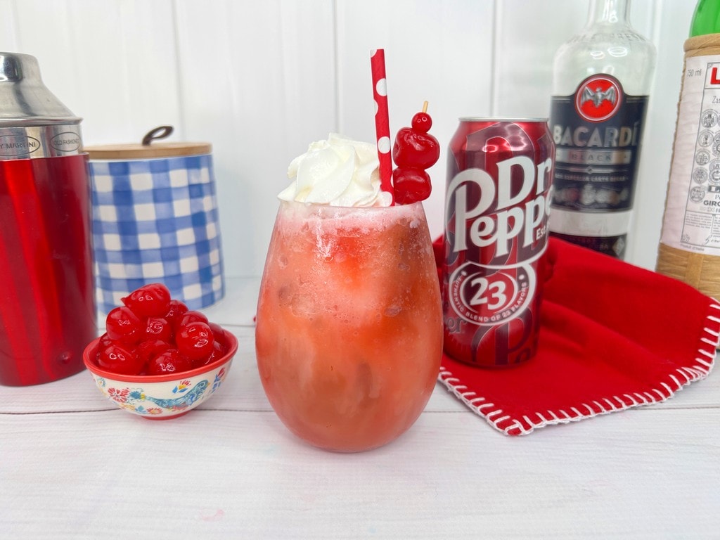 Dirty Dr. Pepper Frozen Rum Slush - Completed red slushy drink with cherries, whip cream and a straw. 