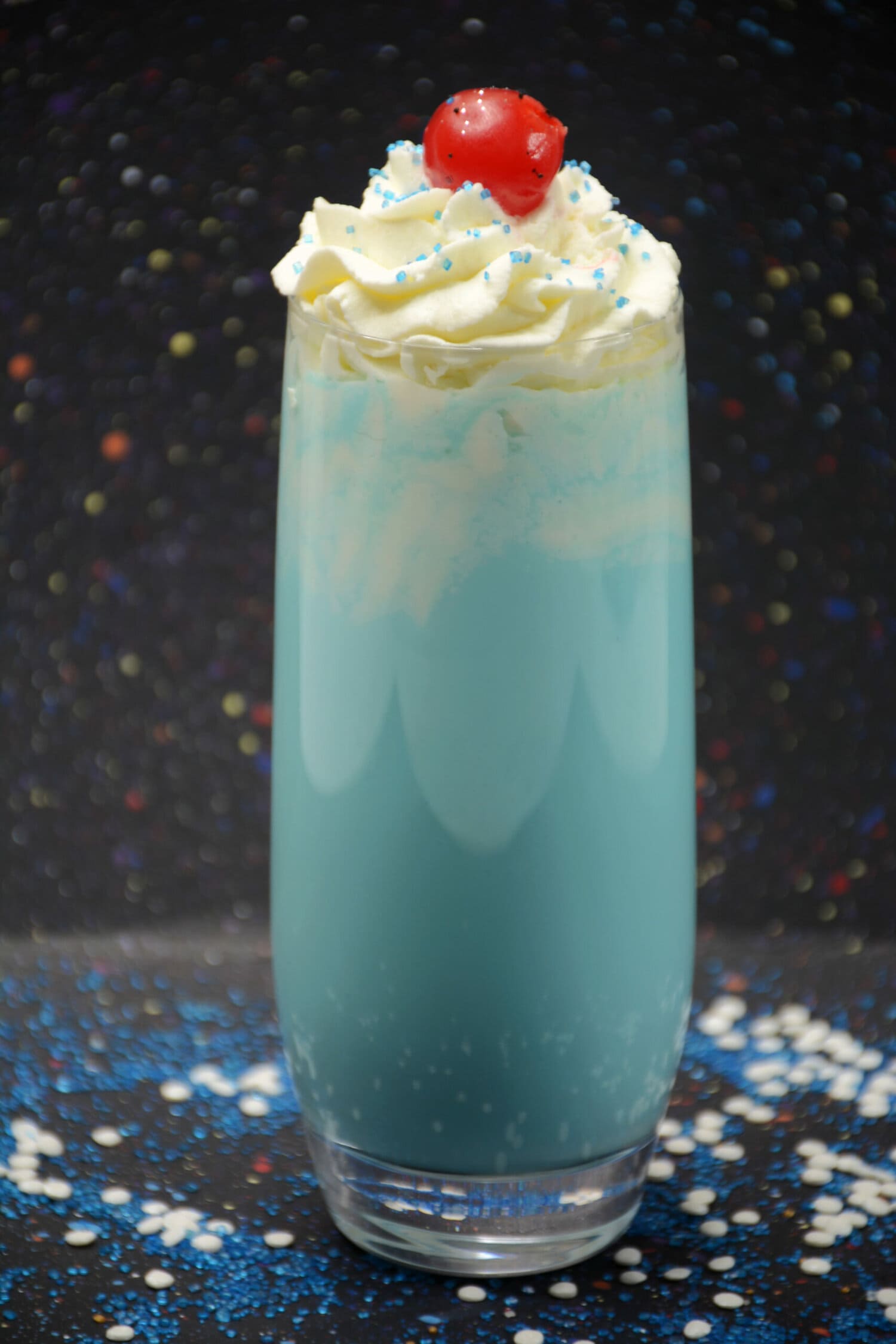 Blue milkshake with whipped topping sprinkles and a cherry in front of a space themed backdrop