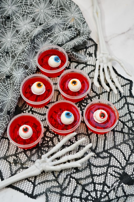 Eyeball Jello Shots - red jello in plastic cups with various colored eyeballs as garnishes. 