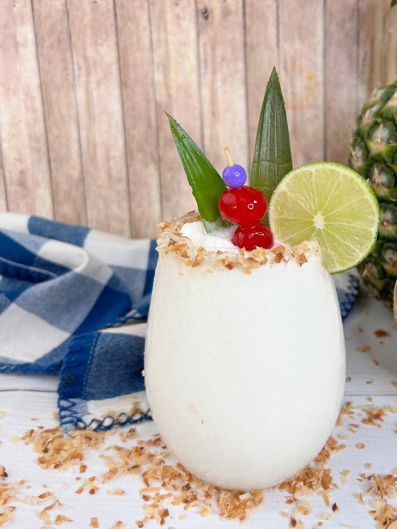 Frozen Brazilian Pina Colada - Close up of white cocktail with toasted coconut on rim. 