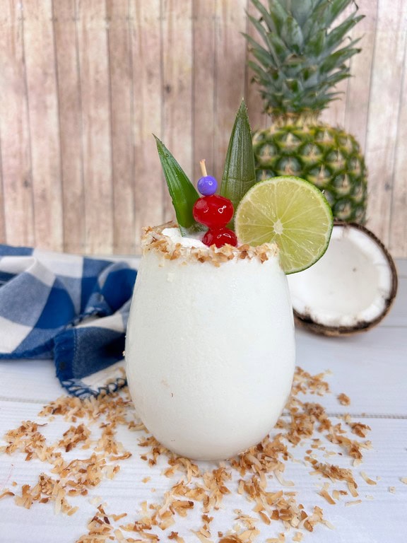 Frozen Brazilian Pina Colada - Completed cocktail with cocnut and pineapple in background. 