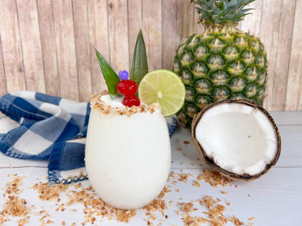 Cocktail with a half coconut and full pineapple in background. 