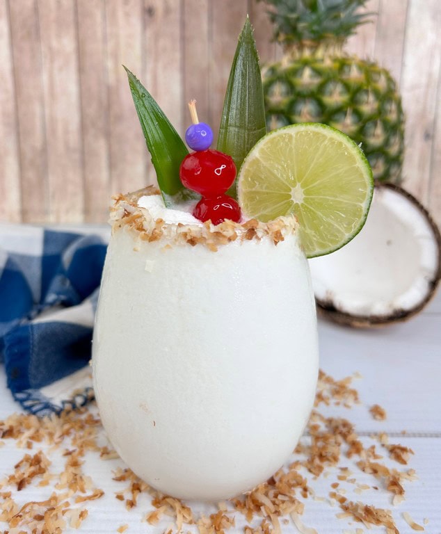 White drink with toasted coconut on rim, with cherries, and lime. 