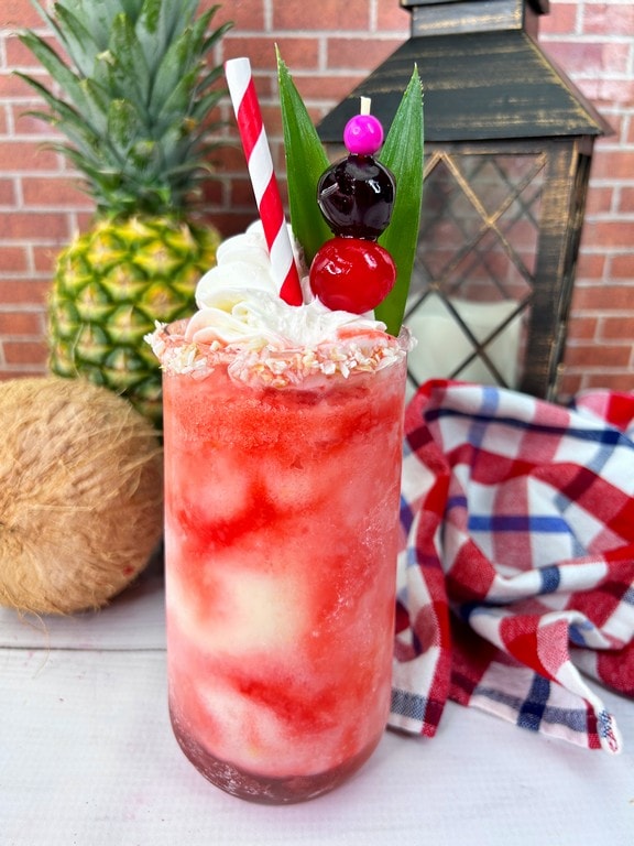 Close up of red cocktail with coconut and pineapple in background. 