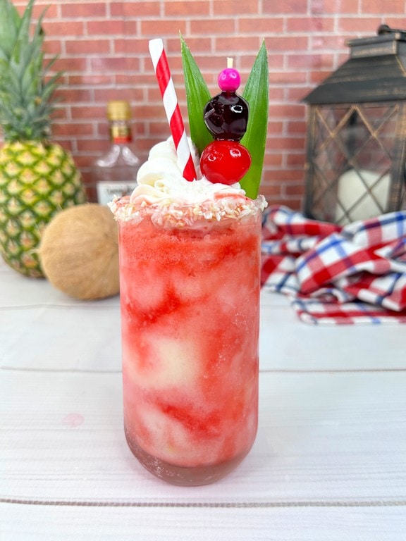 Frozen Cherry Pina Colada - Cocktail with wiped cream, two cherries, pineapple stem leaves and coconut rimmed. 