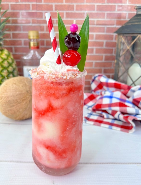 Close up of cocktail with a coconut and pineapple in background. 