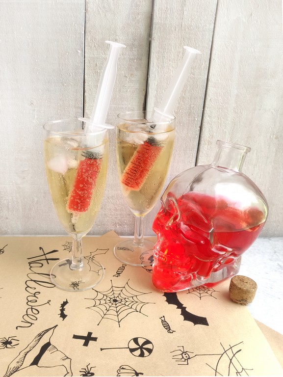 Halloween Mimosa - two completed drinks. Sparkling white wine in tall wine glasses with a syringes in them filled with red grenadine. 