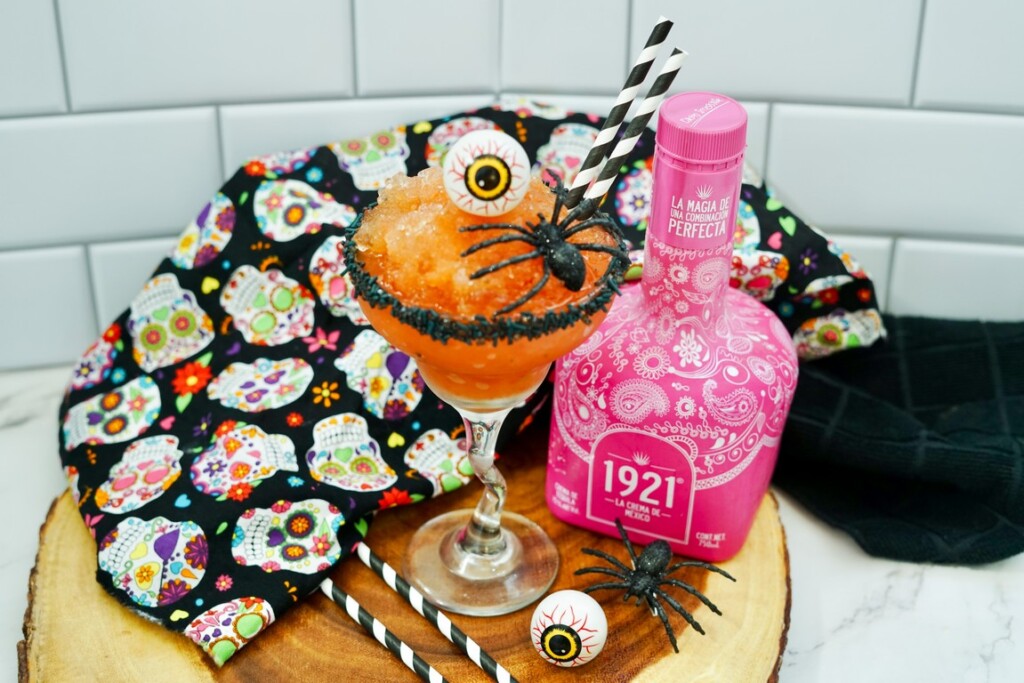 Halloween themed cocktail on wooden slab with plastic spider and eyeballs. 