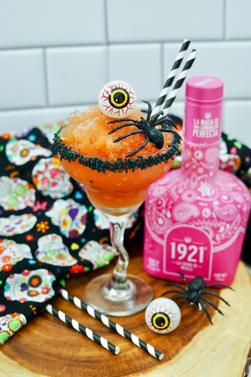 Halloween Strawberry Margarita - close up of margarita with black sprinkles around rim, plastic eye ball and spider. 