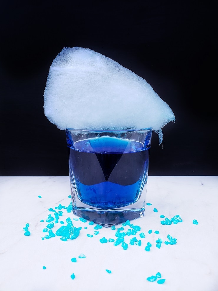 Genie Juice Cocktail, Blue liquid drink in a clear cocktail glass with light blue cotton candy on top. 