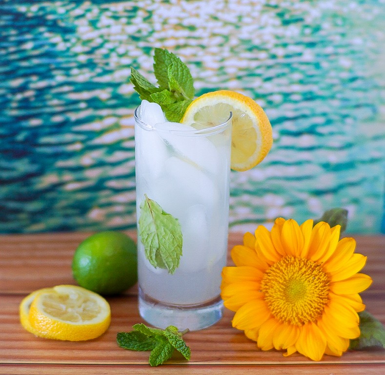 Completed cocktail with sunflowers and limes and lemons by it. 