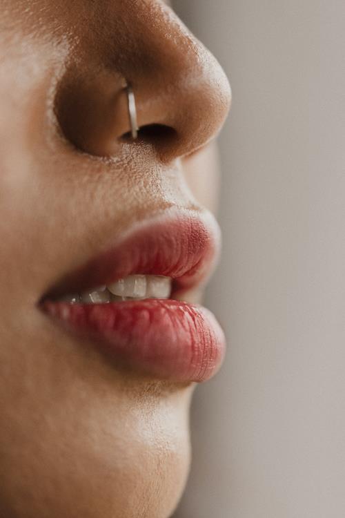 Side view close up of a white woman's face with a silver nose ring, white teeth and pink lips.
