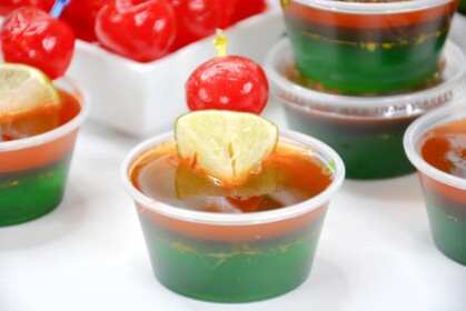 close up showing layers of jello shot, green, red, orange with lime and cherry on top 