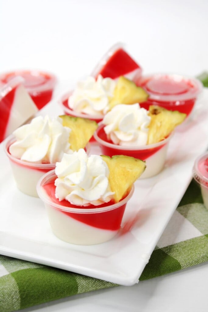 white and red slanted layers with whipped cream and pineapple on top of shot glasses 